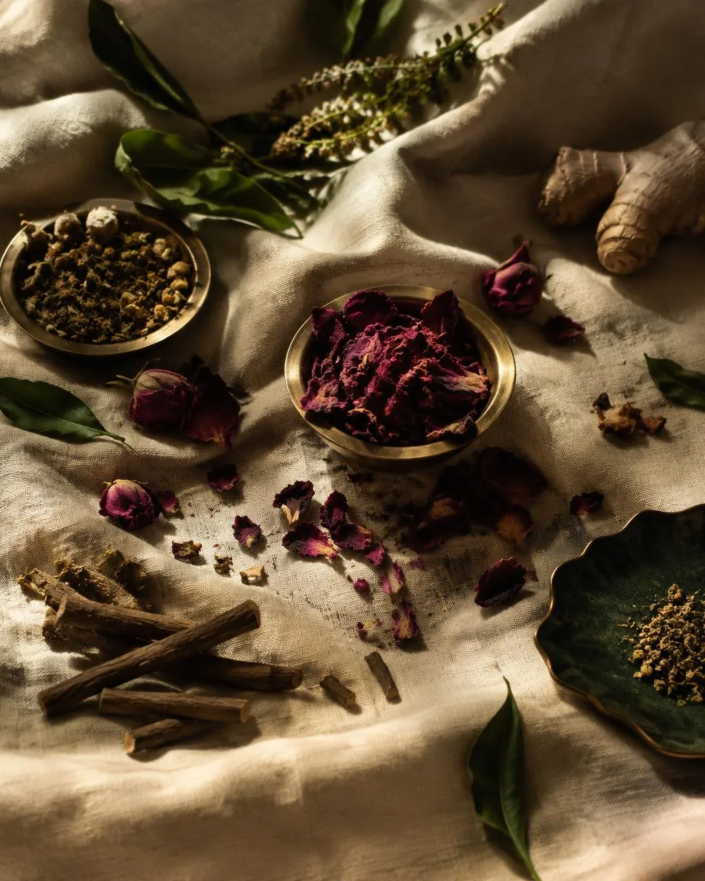 Dried rose petals and ayurvedic herbs in brass bowls on alabaster linen
